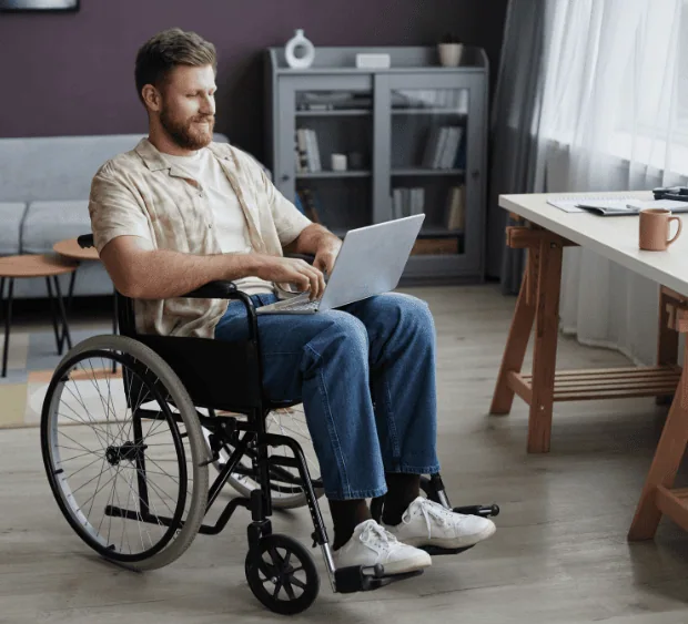 Osoba na wózku inwalidzkim, w domu, pracująca na laptopie